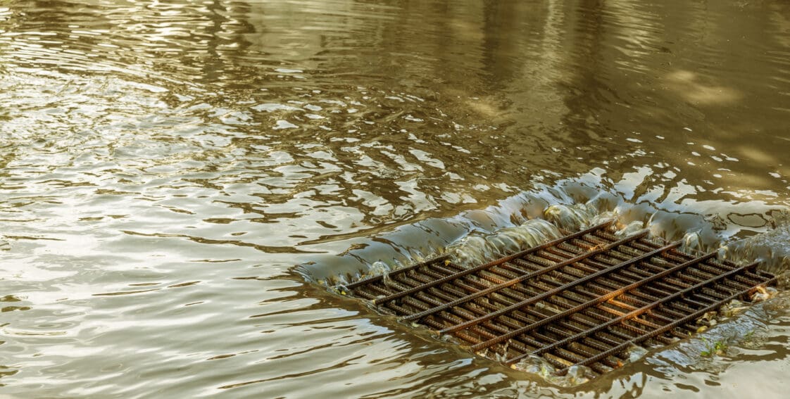 A heavy flow of water flooding a street and running into a stormwater drain.